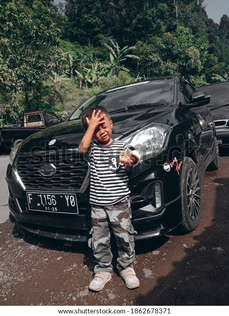 Cianjur, West Java, Indonesia, 27\
November 2020,\
Photo of a small child posing in front of a black\
car in Cianjur, West Java Province, November 17,\
2020