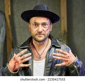 CIEMUPE, LATVIA - JULY 11, 2020: A Man With Bloody Wounds On His Face And Hands In The Old Black Hat And Jacket During Photosession