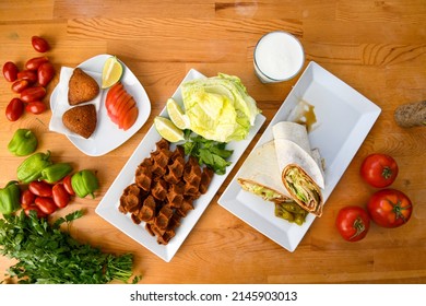 Cig kofte (raw meatball) with lettuce, tomato, pickle and lemon, hot Chee kofta. Turkish local raw food concept.Table scene of assorted take out or delivery foods. Top view of assorted Turkish food.