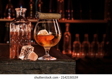 Cigar, elegant glass of brandy on the bar counter. Alcoholic drinks, cognac, whiskey, port, brandy, rum, scotch, bourbon. Vintage wooden table in a pub at night.