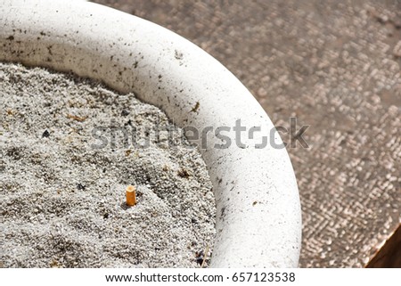 Cigarette butt with ash in the ashtray .