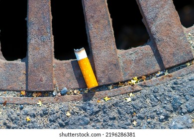 Cigarette butt in the storm sewer cap. The concept of city pollution and the harm of smoking cigarettes. - Shutterstock ID 2196286381