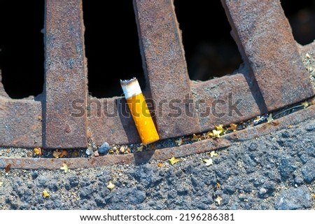 Cigarette butt in the storm sewer cap. The concept of city pollution and the harm of smoking cigarettes.