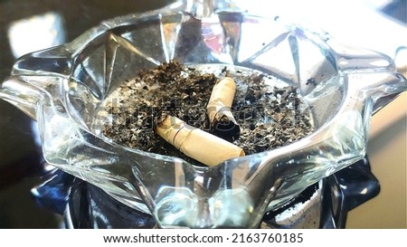 Cigarette butts and cigarette ashes in a glass ashtray