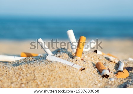 Cigarette butts in yellow sand on sea beach on coast against background of blue sky and sea. Problem of humanity. Cigarette smoking, bad habit. Nicotine addiction. Garbage