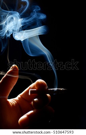 Cigarette in hand with smoke on black background.