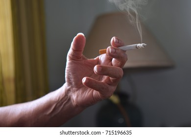 Cigarette In Man Hand With Smoke. Smoking In The House Makes The Air Pollute.