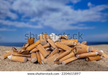 Cigarette stubs dropped and left in a pile on a beautiful beach 