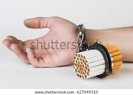 Cigarettes and hand of a man in handcuffs. The concept of nicotine addiction, a bad habit. Isolated on a white background.
