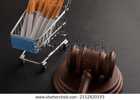 Cigarettes in shopping cart and the judges hammer on black background. Tobacco law. Illegal sale of cigarettes.Ban of cigarettes