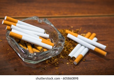 Cigarettes And Tobacco Lying Inside And Around Glass Ash Tray On Wooden Surface, Seen From Above, Anti Smoking Concept