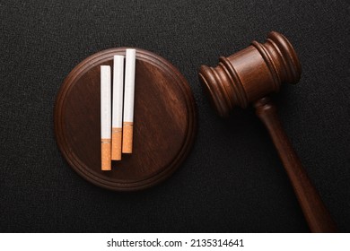 Cigarettes and wooden Judge gavel top view on black background. Violation of the terms of sale of tobacco. Tobacco law - Shutterstock ID 2135314641