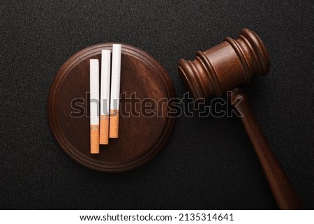 Cigarettes and wooden Judge gavel top view on black background. Violation of the terms of sale of tobacco. Tobacco law