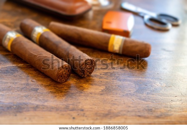 Cigars\
and accessories on a wooden office desk, closeup view. Cuban\
quality cigar tobacco smoking luxury\
lifestyle.