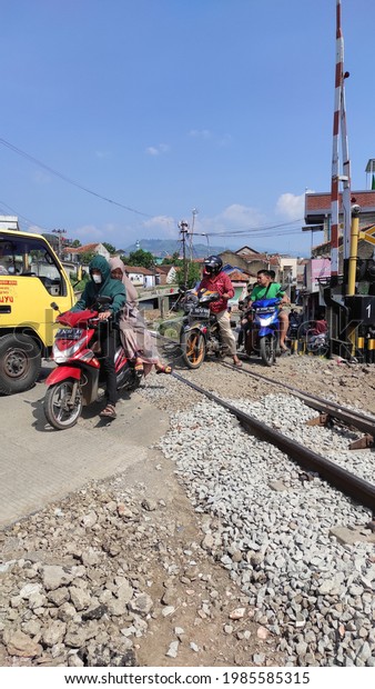 Cikancung, West Java,\
Indonesia - June 04, 2021 : Photo of motorcyclists jostling with\
cars to cross the railroad gates and there are some riders who\
don\'t wear helmets