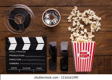 Cinema background, top view. Clapperboard, popcorn, soda and 3D glasses on wooden table. Movie goers accessories, cinematography concept, flat lay