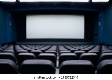 Cinema Hall With White Screen And Black Comfortable Row Chairs For Visitors. Concept Of Empty Cinema Hall.