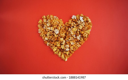 Cinema lovers concept of popcorn. Heart shaped white fluffy popcorn on red background. Saint Valentines day