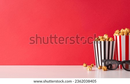 Cinema vibes on display: Side view of striped boxes of cheese and caramel popcorn, 3D glasses adorn white table against a red wall, ready for a premier movie night with friends