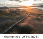 Cinematic aerial image of a car driving on an empty road in the Icelandic highlands with mountains, volcanic lakes during golden hour