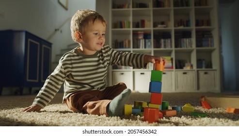 Cinematic authentic shot of active curious toddler baby boy is having fun to play with wooden toy bricks and create towers on carpet in living room at home.