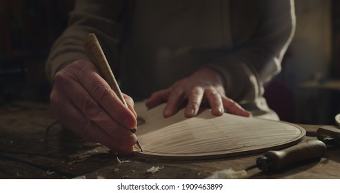 Cinematic close up of master artisan luthier working on creation of handmade fine quality wood violin in creative workshop. Concept of spiritual instrument, handmade, art, orchestra, artisan, music.