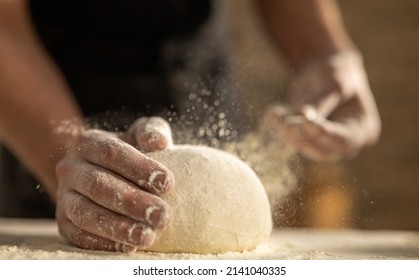 Cinematic close up of professional artisan baker chef sprinkles flour dust powder on fresh just prepared loaf of dough for preparation of pasta, pizza and other pastries in rustic bakery kitchen.