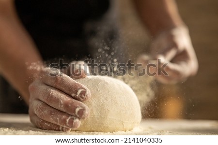 Cinematic close up of professional artisan baker chef sprinkles flour dust powder on fresh just prepared loaf of dough for preparation of pasta, pizza and other pastries in rustic bakery kitchen.