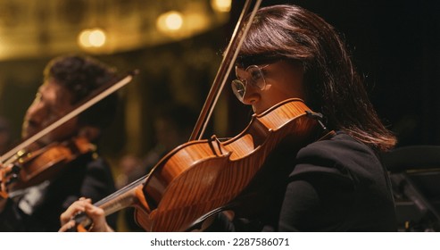 Cinematic Close Up Shot of Professional Symphony Orchestra Violin Player Playing on Classic Theatre with Curtain Stage during Music Concert. Performers Playing Music for Audience - Powered by Shutterstock