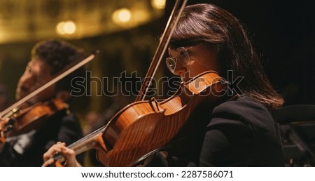Cinematic Close Up Shot of Professional Symphony Orchestra Violin Player Playing on Classic Theatre with Curtain Stage during Music Concert. Performers Playing Music for Audience