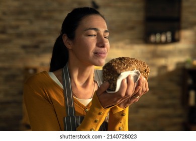 Cinematic close up shot of young female artisan baker is smelling fresh baked bread taken out of oven at moment to control quality in rustic bakery shop kitchen. - Powered by Shutterstock