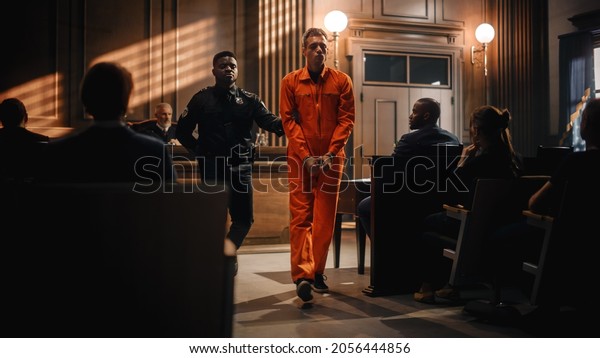 Cinematic Court of Law and Justice Trial
Proceedings: Portrait of Accused Sad Male Criminal in Orange
Jumpsuit Led Away by Security Guard in Front of Judge and Jury.
Sentenced to Serve Jail
Time.