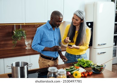 cinematic image of a multiethnic senior couple preparing food in the kitchen. Indoors Lifestyle moments at home. Concept about seniority and relationships - Powered by Shutterstock