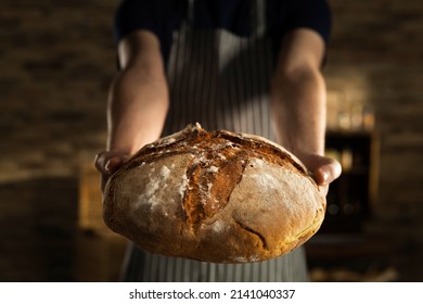 Cinematic macro shot of professional artisan baker is showing in camera just prepared fresh whole grains white bread taken out of oven in rustic bakery kitchen. - Shutterstock ID 2141040337