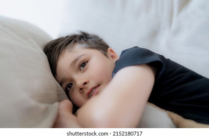 Cinematic Portrait Happy Young Boy Lying On Sofa Looking Out With Smiling Face,Positive Child Resting In Living Room With Bright Light Shining On Spring Or Summer. Kid Relaxing Watching TV On Weekend