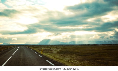 A Cinematic Road In Iceland With Magical Sun Rays Peaking Through The Clouds In The Background. 