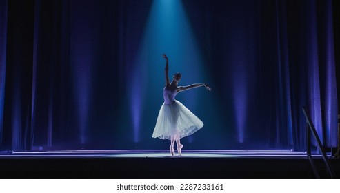 Cinematic Shot of Ballerina in Pointe Shoes and White Tutu Dancing and Rehearsing on Classic Theatre Stage with Dramatic Lighting. Graceful Classical Ballet Female Dancer Performing a Choreography - Powered by Shutterstock