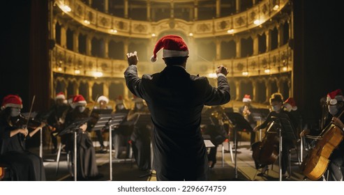 Cinematic shot of Conductor Directing Symphony Orchestra with Performers All Wearing Santa Hats Playing Violins, Cello and Trumpet on Classic Theatre with Curtain Stage During Christmas Music Concert - Shutterstock ID 2296674759