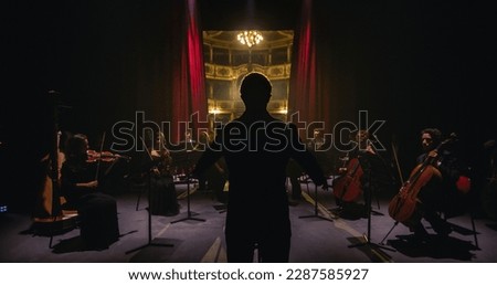 Cinematic shot of Curtains Opening Revealing a Conductor Directing the Beginning of Symphony Orchestra Show with Performers Playing Violins, Cello and Trumpet on Classic Theatre During Music Concert