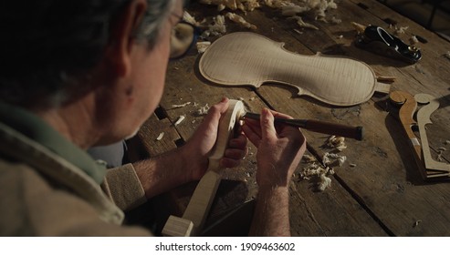 Cinematic shot of experienced master artisan luthier painstaking detail work on fine quality wood violin in creative workshop.Concept of spiritual instrument,handmade, art, orchestra, artisan, passion