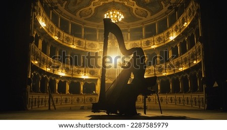 Cinematic shot of Female Harpist Playing Harp Solo on an Empty Classic Theatre Stage with Dramatic Lighting. Professional Musician Rehearsing Before the Start of a Big Show. Silhouette Aesthetics