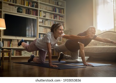Cinematic shot of happy smiling mature senior couple doing exercises of gymnastics together at home. Concept of healthy lifestyle, fitness, recreation, couple goals, well being, retirement, elderly.