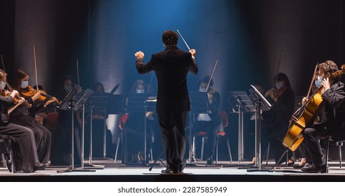 Cinematic Shot of an Orchestra on a Classic Theatre Stage: Professional Conductor Directing Symphony Orchestra with Performers Playing Violins, Cellos, and Trumpets During Music Concert