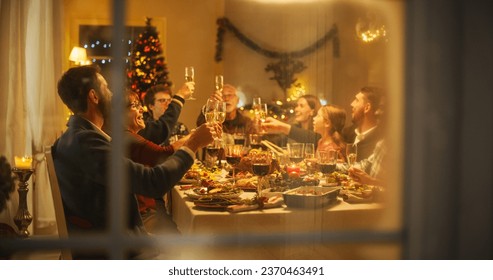 Cinematic Shot Through a Snowy House Window: Christmas Dinner Together with Parents, Children and Friends at Home. Multicultural Family Raising Champagne Glasses and Toasting, Celebrating Holidays - Powered by Shutterstock