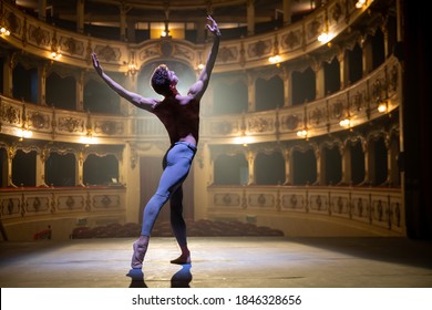 Cinematic shot of an young athletic classical ballet male dancer is performing a choreography on a classic theatre stage with dramatic lighting before start of a show.