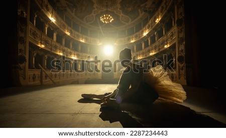 Cinematic Shot of a Young Classical Ballet Female Dancer Putting on her Pointe Shoes on a Stage of Classic Theatre . Graceful Ballerina Getting Ready for the Performance. Silhouette Aesthetic Shot