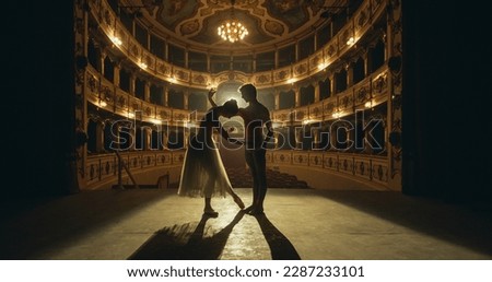 Cinematic shot of Young Couple of Classical Ballet Dancers Performing on the Stage of Classic Theatre with Dramatic Lighting. Male and Female Dancers Rehearse their Performance Together Before a show