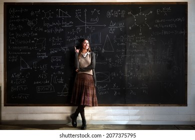 Cinematic shot of young female teacher or student indicates with forefinger at blackboard with math formulas and equations and smiles in camera in college or university classroom. - Powered by Shutterstock