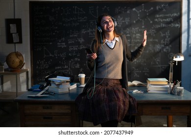 Cinematic shot of young happy female teacher or student with headphones is having fun to listen music with smartphone and dance in front of blackboard with formulas in college or university classroom. - Powered by Shutterstock - Get 15% off with code: PIKWIZARD15