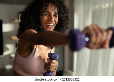 Cinematic shot of young happy smiling sporty brazilian woman with athletic body wearing bra and leggings is practicing high intensity cardio exercises with dumbbells at home. - Powered by Shutterstock